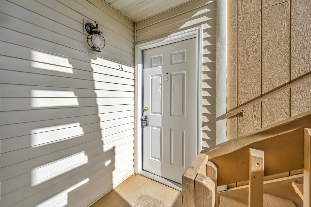 White exterior front door with siding and wooden railing